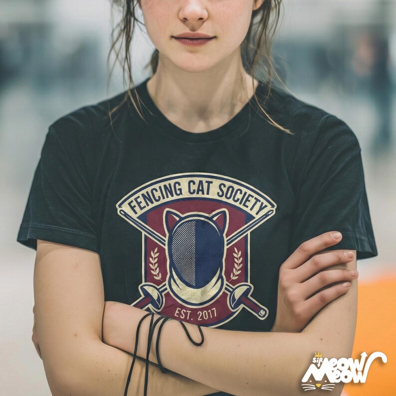 May include: Black t-shirt featuring the text "FENCING CAT SOCIETY" above a fencing mask design, crossed swords, and the text "EST. 2017". The shirt also has a small logo of a cat wearing a crown.