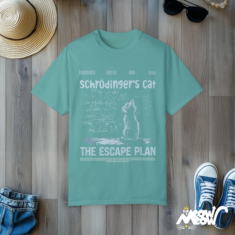 May include: A teal blue t-shirt with a white graphic of a cat looking up at a chalkboard with equations and the text "Schr&ouml;dinger's cat The Escape Plan".