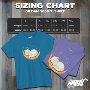 Op de afbeelding: Twee t-shirts, &eacute;&eacute;n turquoise en &eacute;&eacute;n paars, met een witte kat die slaapt op een maan met sterren. Boven staat een maattabel voor een Gildan 5000 t-shirt. De afmetingen zijn in centimeters.