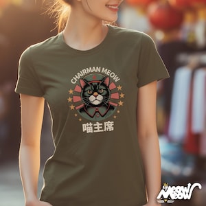 May include: Olive green t-shirt featuring a cartoon cat wearing a military-style uniform and a black hat. The text "CHAIRMAN MEOW" arches above the cat, with Chinese characters below. The design includes red stars and a circular emblem.