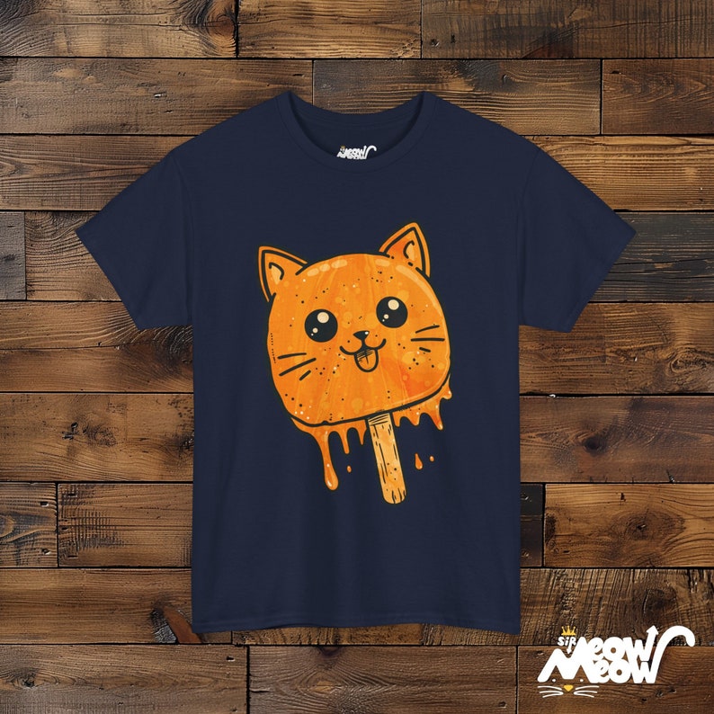 May include: A navy blue t-shirt with a cartoon orange cat popsicle graphic. The cat has a tongue sticking out and dripping orange ice cream.