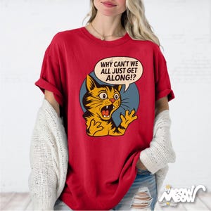 May include: Red t-shirt featuring a cartoon cat with an open mouth and the text "WHY CAN'T WE ALL JUST GET ALONG!?" in a speech bubble. The cat is yellow and black, set against a blue circle.