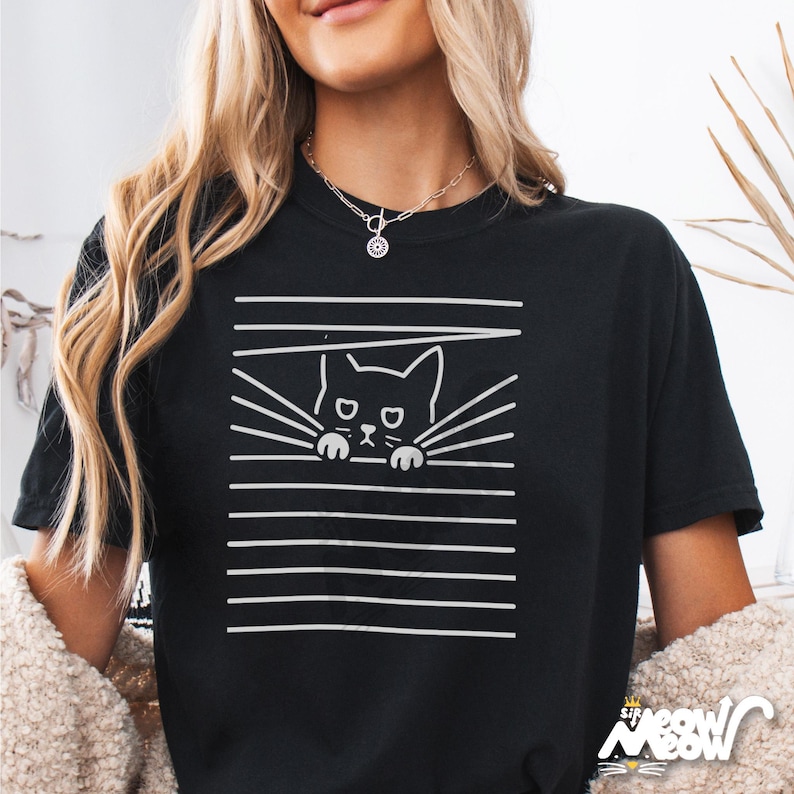 May include: Black t-shirt with a white graphic of a cat peeking through blinds. The cat has a sad expression and is looking directly at the viewer.