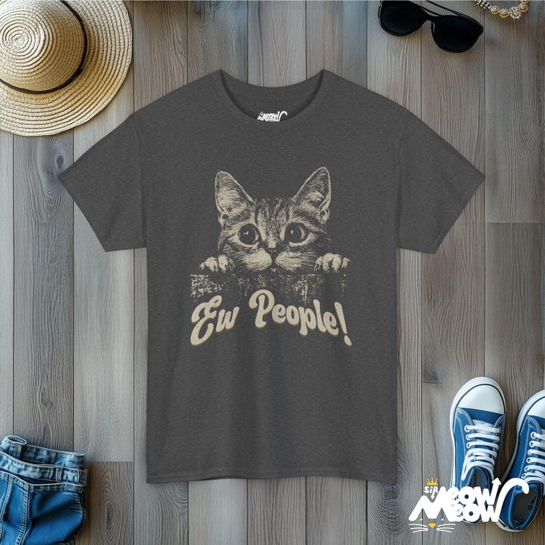 Puede incluir: Una camiseta gris oscuro con un gr&aacute;fico de un gato mirando por encima de una pared y el texto "Ew People!" impreso en la parte delantera.