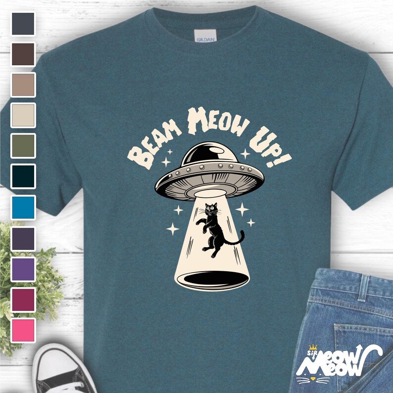 May include: A teal blue t-shirt with a graphic of a black cat being beamed up in a flying saucer. The text "Beam Meow Up!" is printed on the shirt.