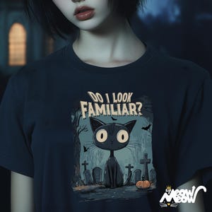 May include: A dark blue t-shirt with a black cat illustration and the text "Do I look familiar?" The cat is in a graveyard setting with tombstones and bats.