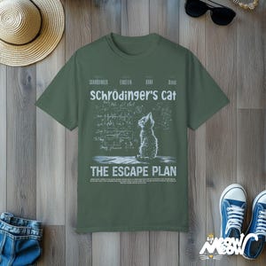 May include: A green t-shirt with a white graphic of a cat looking up at a chalkboard filled with equations and the text "Schr&ouml;dinger's Cat The Escape Plan".