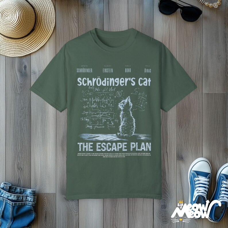 May include: A green t-shirt with a white graphic of a cat looking up at a chalkboard filled with equations and the text "Schr&ouml;dinger's Cat The Escape Plan".