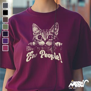 Puede incluir: Camiseta color burdeos con un gr&aacute;fico de un gato asom&aacute;ndose por encima de una pared y el texto "Ew People!" impreso en blanco.