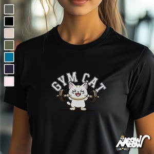 Könnte beinhalten: Schwarzes T-Shirt mit einer weißen Comic-Katze, die Gewichte hebt. Der Text "Gym Cat" befindet sich über der Katze.