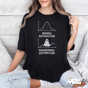 Op de afbeelding: Zwart T-shirt met een humoristische afbeelding. Het ontwerp bevat een grafiek met het label "Normale verdeling" en een andere met het label "Paranormale verdeling" met een spookpictogram. Een casual kledingstuk.