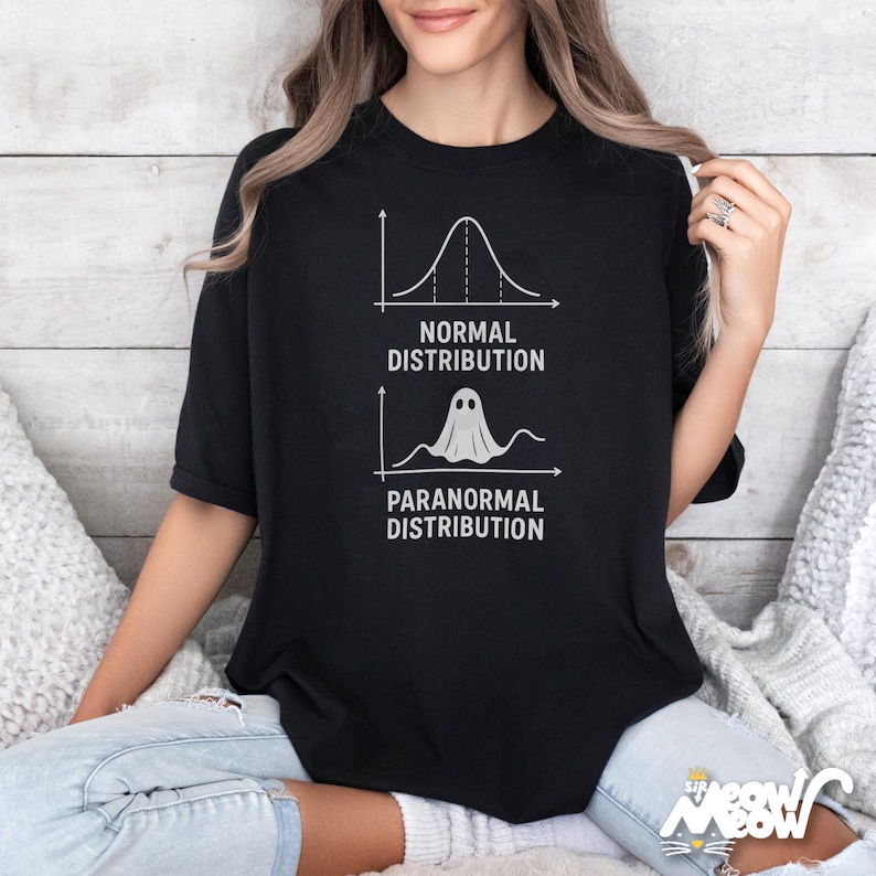 Op de afbeelding: Zwart T-shirt met een humoristische afbeelding. Het ontwerp bevat een grafiek met het label "Normale verdeling" en een andere met het label "Paranormale verdeling" met een spookpictogram. Een casual kledingstuk.