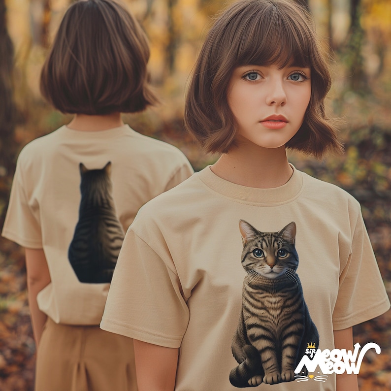 Girl with bobbed brown hair in the forest. She is wearing a t-shirt with a tabby cat on the front, and the back of the tee shows the back of the tabby cat.