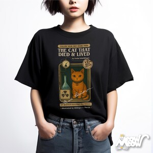May include: Black t-shirt with a vintage book cover design featuring a cat in a science experiment. The text reads "The Cat That Died & Lived" by Erwin Schr&ouml;dinger. #1 Best Seller. 15 Quantum Outcomes to Fur-Sue! Illustrated by Hildegunte March.