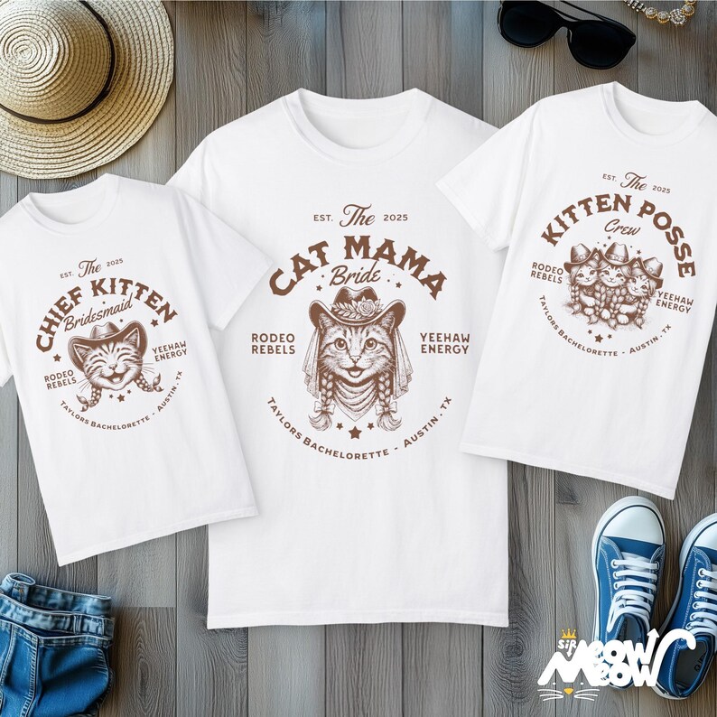 May include: Three white t-shirts with brown graphic designs. One shirt says "Cat Mama Bride," another says "Chief Kitten Bridesmaid," and the third says "Kitten Posse Crew." The shirts have a western theme with cat illustrations.