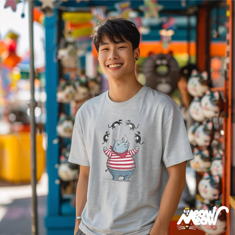 May include: A gray t-shirt with a cartoon illustration of a rhinoceros wearing a striped shirt and juggling black cats. The shirt has a relaxed fit and a crew neck.