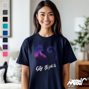 Pode incluir: Uma camiseta azul marinho com um gr&aacute;fico de uma silhueta de gato preto com um horizonte da cidade dentro. O texto "City Nights" &eacute; impresso abaixo do gr&aacute;fico.