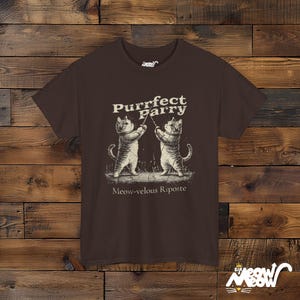 May include: A brown t-shirt with a graphic of two cats fencing. The text on the shirt reads "Purrfect Parry Meow-velous Riposte".