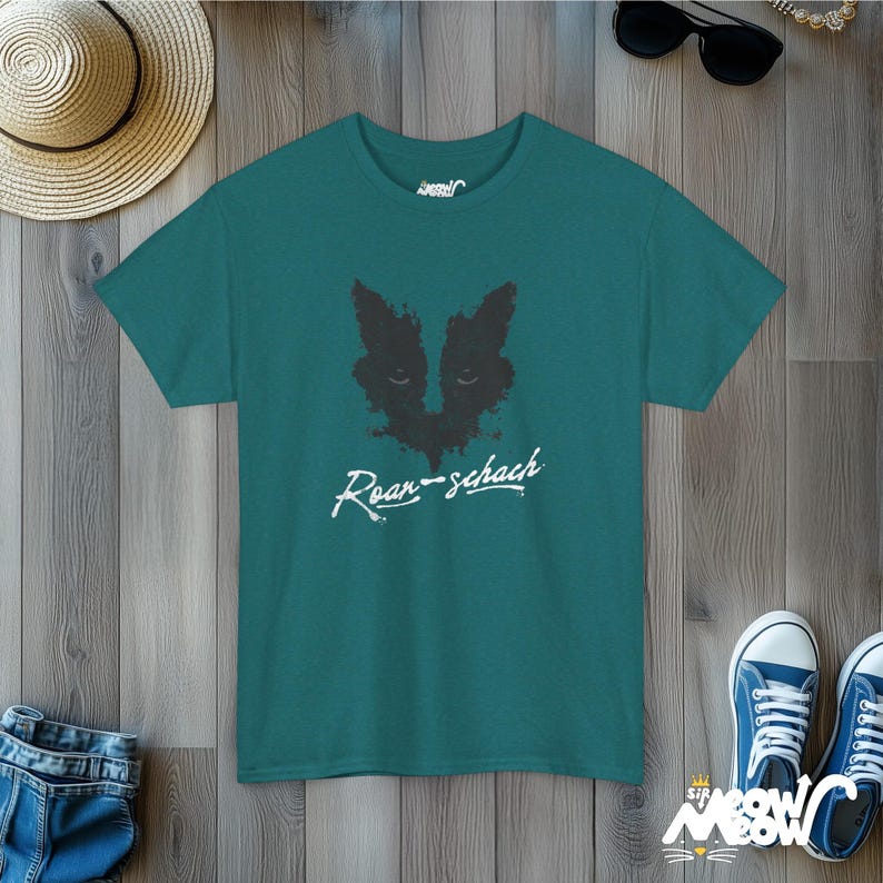 May include: Teal blue t-shirt with a black inkblot design resembling a cat's face and the text "Roar-schach" in white.
