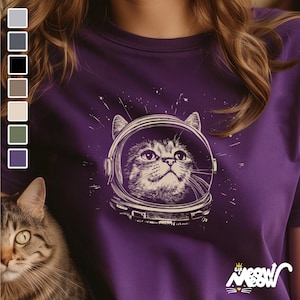 May include: Purple t-shirt with a graphic of a cat wearing an astronaut helmet. The cat is looking up and the graphic is surrounded by stars. The text "Sir Meow" is printed on the bottom right corner of the shirt.