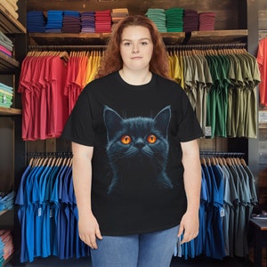 May include: Black t-shirt featuring a detailed illustration of a black cat with bright orange eyes. The cat's fur is dark, contrasting with the vibrant eyes. The shirt is a classic crew neck style, suitable for casual wear.
