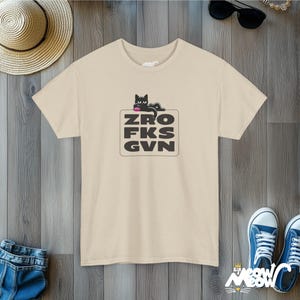 Pode incluir: Uma camiseta bege com uma ilustra&ccedil;&atilde;o de um gato preto e o texto "ZRO FKS GVN" impresso na frente.