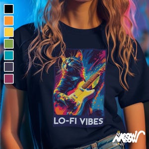 May include: Navy blue t-shirt featuring a colorful illustration of a cat playing an electric guitar. The graphic has a vibrant, abstract style with the text "LO-FI VIBES" below. The shirt also has a small logo at the bottom right.