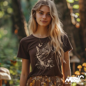 Vintage style t-shirt print of a cat in the woodlands surrounded by wildflowers, mushrooms and butterflies. Chocolate brown tee worn by a pretty blonde woman in a forest.