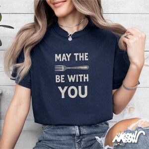 Peut inclure: T-shirt bleu marine avec l'inscription "MAY THE FORK BE WITH YOU" en blanc, dans une police de style vintage. Le design comprend une illustration de fourchette. Un v&ecirc;tement d&eacute;contract&eacute; pour tous les jours.