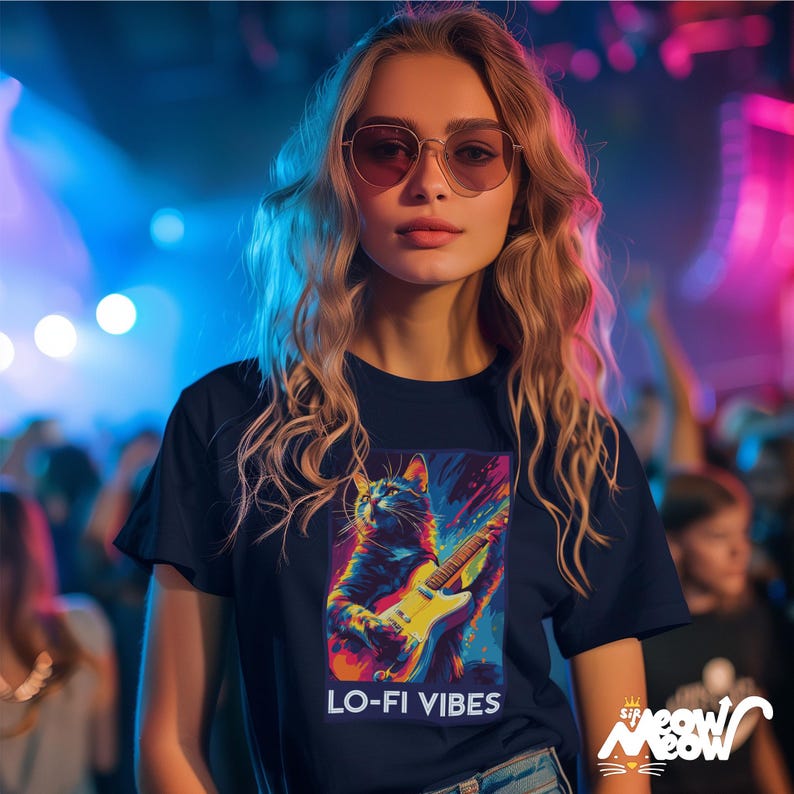 May include: Navy blue t-shirt featuring a colorful illustration of a cat playing an electric guitar, with the text "LO-FI VIBES". The shirt has a vibrant, artistic design and is part of the "Sip Meow Meow" collection.