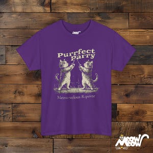 May include: Purple t-shirt with a graphic of two cats fencing. The text on the shirt reads "Purrfect Parry" and "Meow-velous Riposte".
