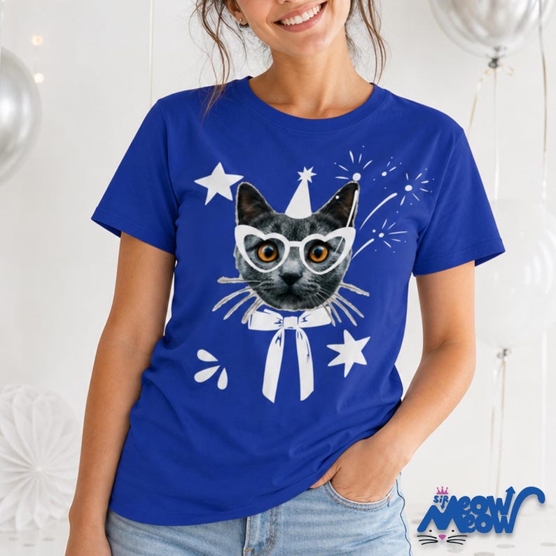 Puede incluir: Camiseta azul real con un dise&ntilde;o de gato con gafas, gorro de fiesta y pajarita. Estrellas blancas y fuegos artificiales rodean el gato. El texto "Sip Meow" est&aacute; en la parte inferior derecha.