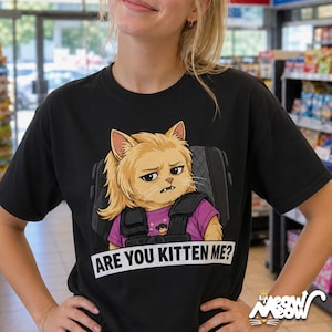 K&ouml;nnte beinhalten: Schwarzes T-Shirt mit einer Cartoon-Katze mit blonden Haaren und einem ernsten Gesichtsausdruck, die ein lila Hemd und eine taktische Weste tr&auml;gt. Der Text "ARE YOU KITTEN ME?" ist darunter gedruckt.
