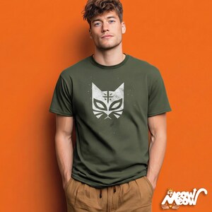 May include: Olive green t-shirt featuring a white cat mask design. The graphic has a distressed, vintage look. The shirt is short-sleeved and has a crew neck. The brand logo "Sir Meow Meow" is visible in the bottom right corner.