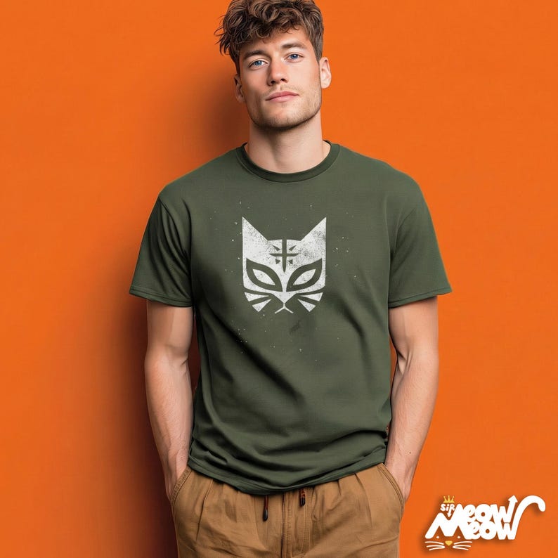 May include: Olive green t-shirt featuring a white cat mask design. The graphic has a distressed, vintage look. The shirt is short-sleeved and has a crew neck. The brand logo "Sir Meow Meow" is visible in the bottom right corner.