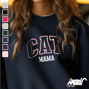 May include: A navy blue sweatshirt with the text "CAT MAMA" in white with red outlining. The sweatshirt has a crew neck and long sleeves.