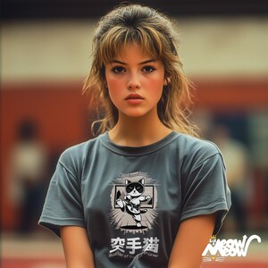 May include: A woman wearing a gray t-shirt with a black and white illustration of a cat doing karate. The text on the shirt says "Master of the Paw" and "空手猫".