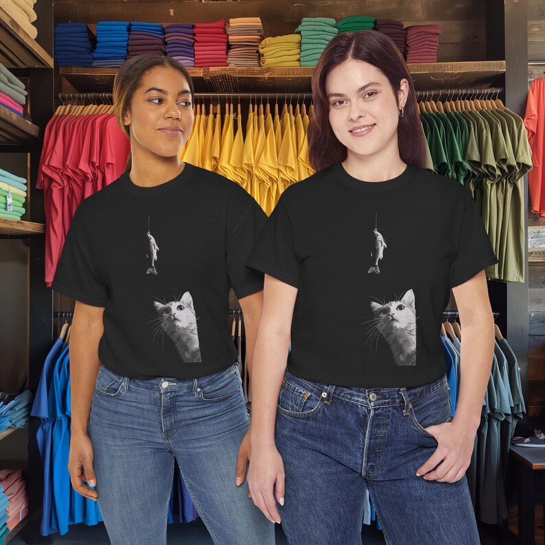 May include: Two people wearing black t-shirts with a white cat and fish graphic. The cat is looking up at the fish on a fishing line.