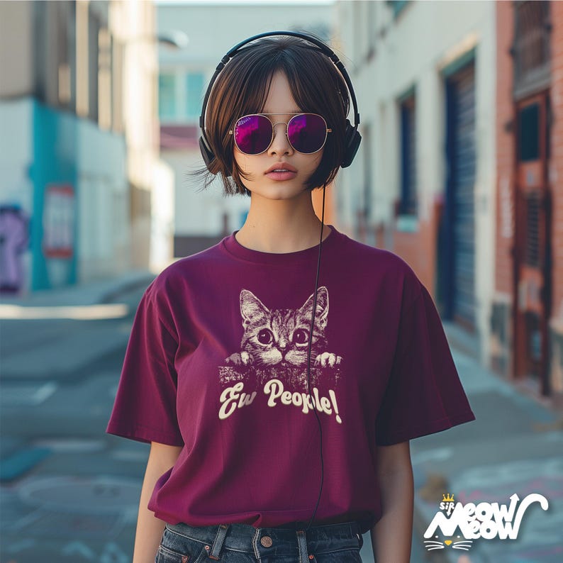 Puede incluir: Una camiseta de color granate con un gr&aacute;fico de un gato asom&aacute;ndose por encima de una superficie y el texto "Ew People!" impreso en la parte delantera.