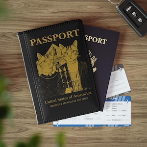 以下が含まれることがあります： 金色の文字と猫のイラストが入った黒いパスポートカバー。「PASSPORT」と「United States of Ameowica, Midwest Mewseum Edition」と書かれています。青いパスポートと航空券も表示されています。