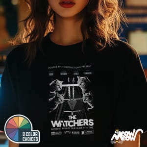 May include: Black t-shirt with a white graphic of a movie poster for "The Watchers" featuring a group of cats. The poster text reads "Double-Split Productions Present" and "Altering Reality One Blink At A Time". The poster also includes a Dolby logo and an R rating.