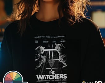May include: Black t-shirt with a white graphic of a movie poster for "The Watchers" featuring a group of cats. The poster text reads "Double-Split Productions Present" and "Altering Reality One Blink At A Time". The poster also includes a Dolby logo and an R rating.