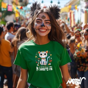 May include: A green t-shirt with a colorful cat design, the words "Dia de los Muertos" are printed below the cat. The person in the image is smiling and wearing face paint and a decorative headpiece. The background is a crowded street scene.