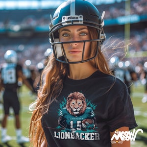 May include: A woman wearing a black t-shirt with a graphic of a lion wearing a football jersey and holding a football. The text on the shirt reads "Linebacker 15" and "Lionbacker".