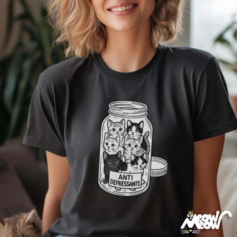 May include: Black t-shirt featuring a jar filled with several cartoon cats. The jar has a white label that reads "ANTI DEPRESSANTS". The shirt has a round neck and short sleeves. The image is a playful design.