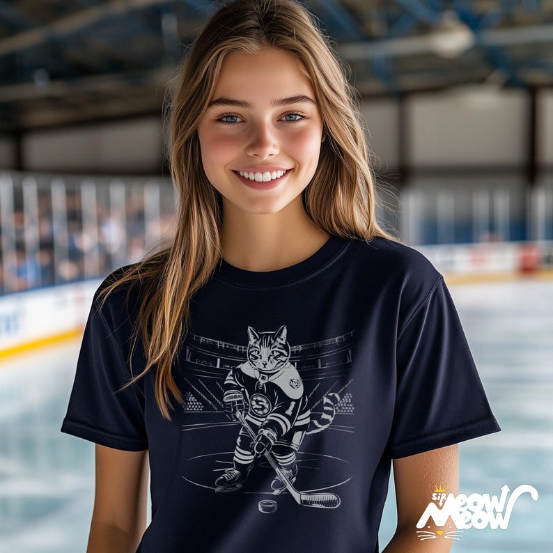 Op de afbeelding: Een vrouw draagt een donkerblauw t-shirt met een afbeelding van een kat die hockey speelt. De kat draagt een hockeytrui met nummer 31. De afbeelding is in zwart-wit en de tekst op het shirt zegt "Sir Meow Meow".