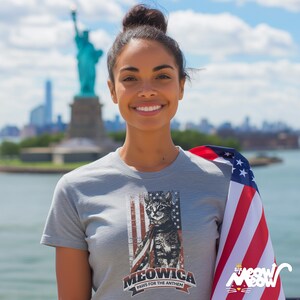 May include: A gray t-shirt with a graphic of a cat wearing a small American flag. The text on the shirt reads "Meowica Paws for the Anthem".