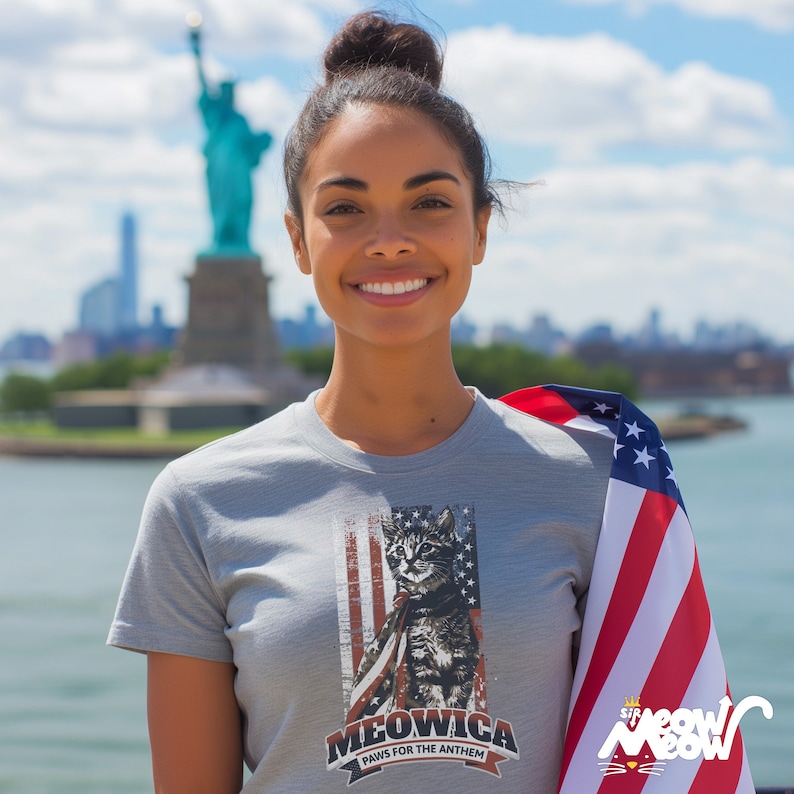 May include: A gray t-shirt with a graphic of a cat wearing a small American flag. The text on the shirt reads "Meowica Paws for the Anthem".