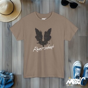 May include: A brown t-shirt with a black and white graphic of a cat's face and the text "Roar-schach" printed on the front.