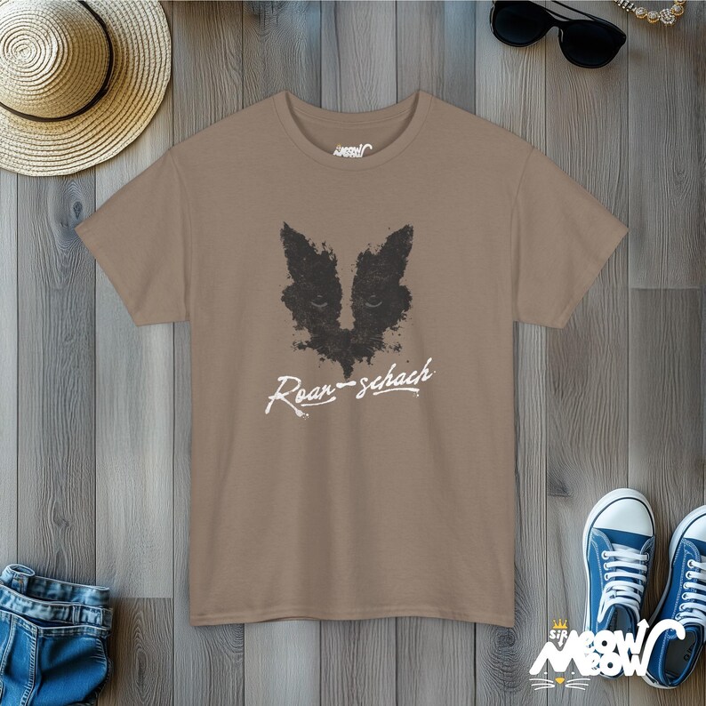 May include: A brown t-shirt with a black and white graphic of a cat's face and the text "Roar-schach" printed on the front.